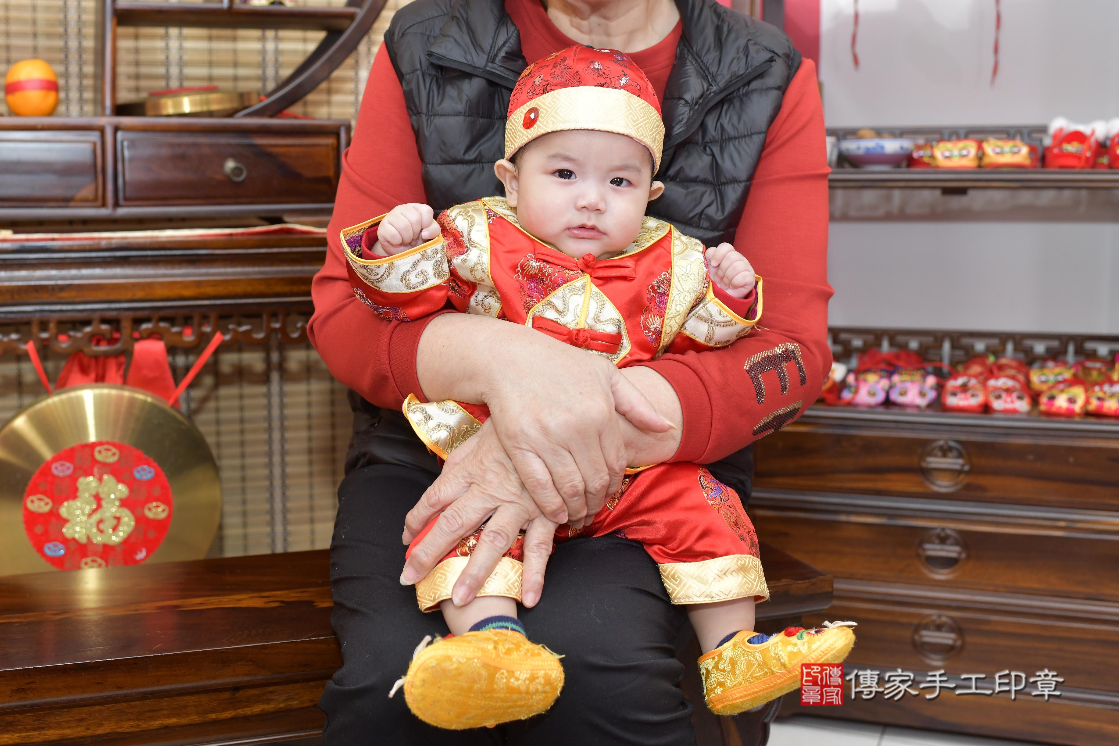 一家人一起穿著一套刺繡精美的紅色唐裝，笑容甜美，萌態十足。 這樣的傳統服飾，不僅為儀式增添了文化色彩，也讓這一天的紀念照片更加生動。